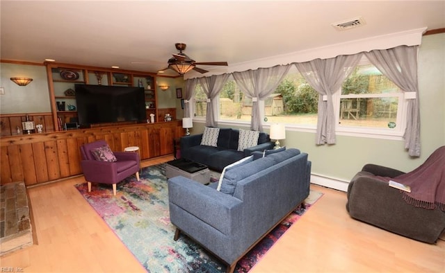 living area featuring ceiling fan, wood finished floors, visible vents, baseboard heating, and crown molding