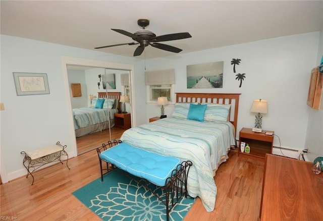 bedroom featuring wood finished floors, a ceiling fan, baseboards, a closet, and baseboard heating