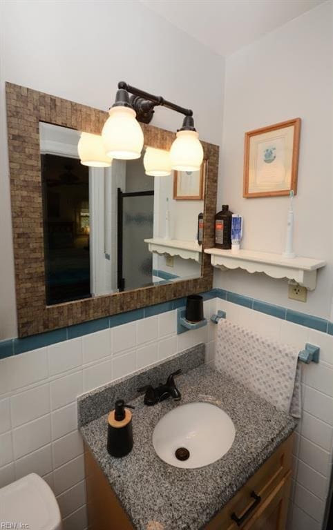 bathroom featuring toilet, wainscoting, tile walls, and vanity