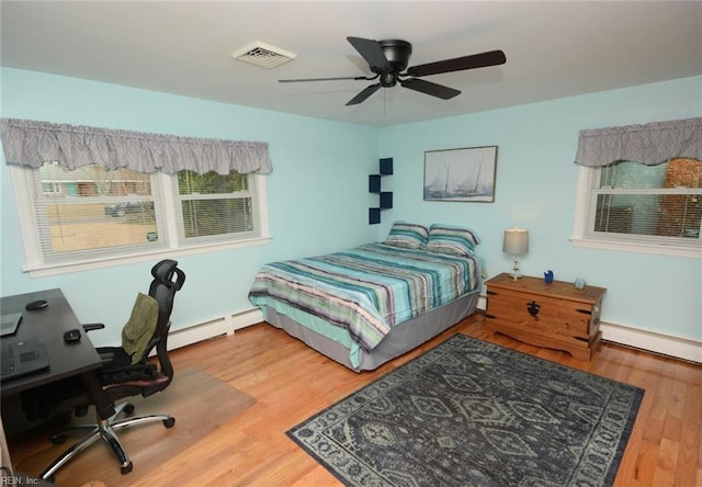 bedroom featuring a baseboard heating unit, a ceiling fan, visible vents, and wood finished floors