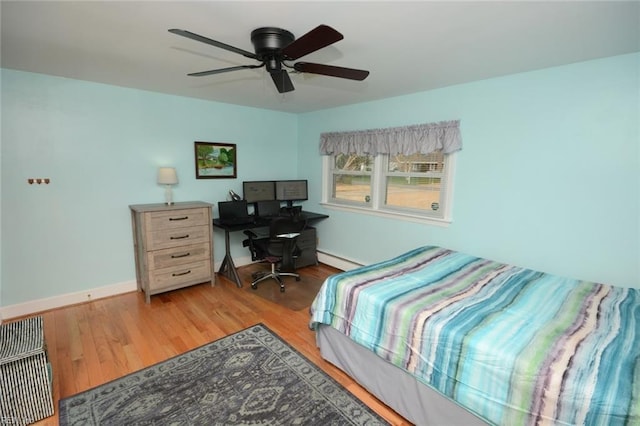 bedroom featuring a baseboard heating unit, ceiling fan, baseboards, and wood finished floors