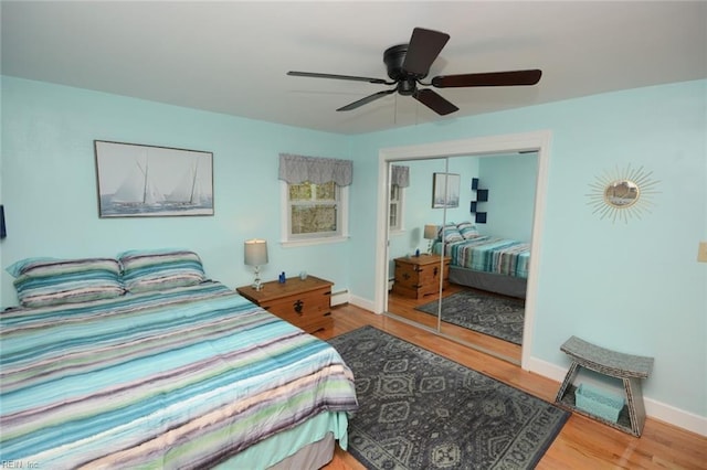 bedroom with ceiling fan, a baseboard radiator, wood finished floors, baseboards, and a closet