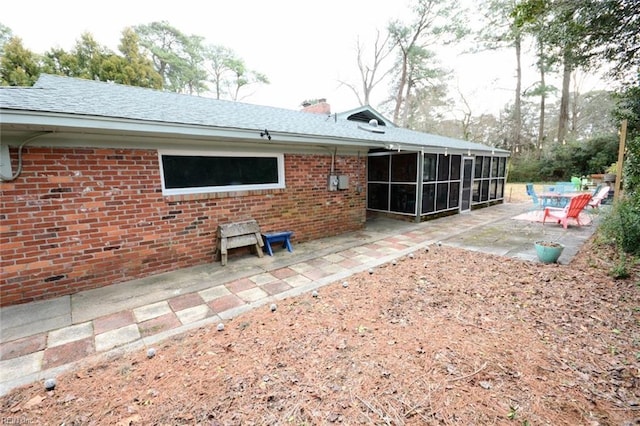 rear view of house featuring brick siding, roof with shingles, a chimney, a sunroom, and a patio area