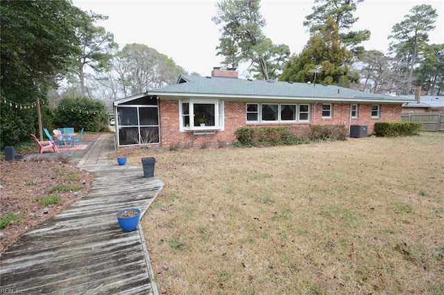 rear view of house with brick siding, a chimney, a lawn, central AC unit, and a sunroom