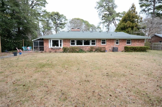 back of house with a sunroom, a chimney, a lawn, and brick siding