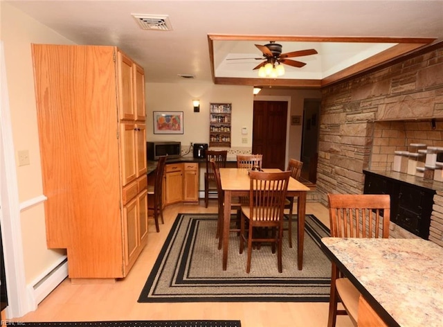 dining space with a stone fireplace, a baseboard radiator, visible vents, a ceiling fan, and light wood finished floors