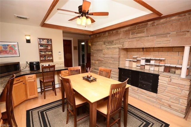 dining space featuring light wood finished floors, visible vents, ceiling fan, a stone fireplace, and built in desk