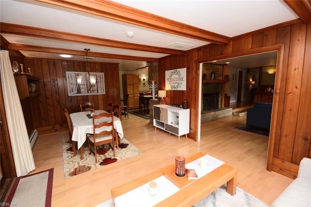 dining room with a baseboard radiator, an inviting chandelier, light wood-style floors, wood walls, and beamed ceiling