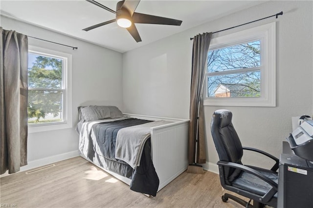 bedroom with a ceiling fan, visible vents, baseboards, and wood finished floors