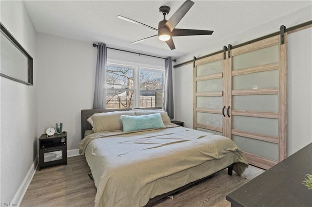 bedroom with a textured ceiling, a barn door, wood finished floors, a ceiling fan, and baseboards