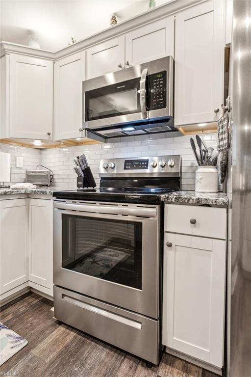 kitchen with stainless steel appliances, white cabinets, decorative backsplash, dark wood-style floors, and dark stone countertops