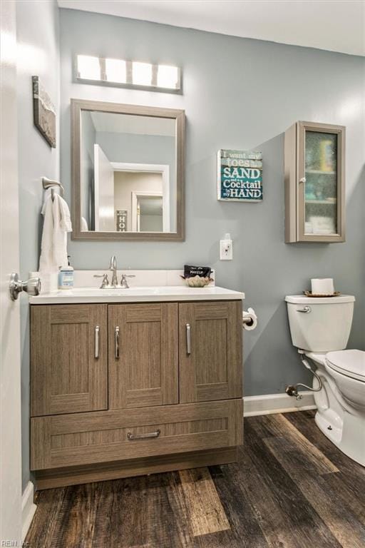 half bath with vanity, wood finished floors, toilet, and baseboards