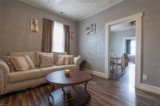 living area featuring baseboards, visible vents, a textured wall, ornamental molding, and wood finished floors