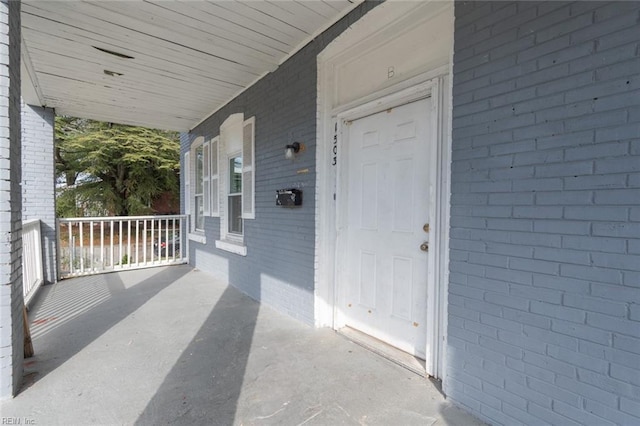 entrance to property featuring a porch and brick siding