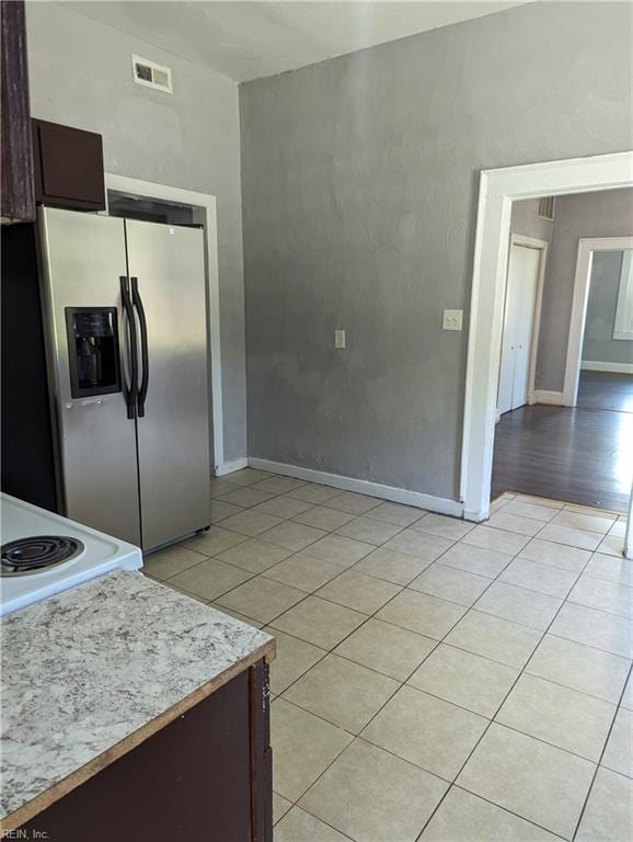 kitchen with light tile patterned floors, visible vents, light countertops, dark brown cabinets, and stainless steel fridge