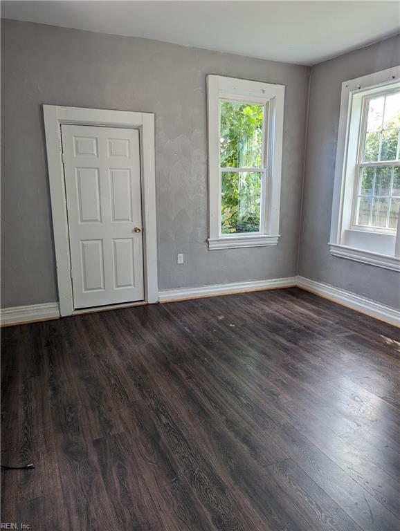 spare room featuring dark wood-type flooring, a healthy amount of sunlight, and baseboards