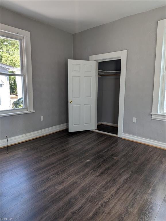 unfurnished bedroom with a closet, baseboards, and dark wood-style flooring