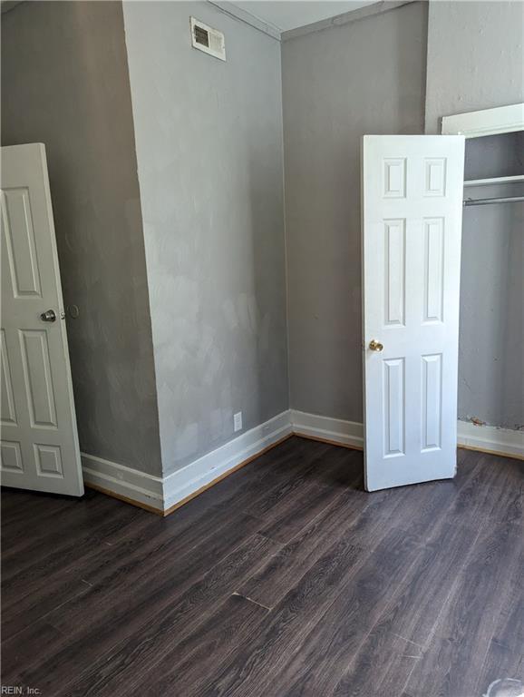 empty room featuring dark wood-type flooring, visible vents, and baseboards