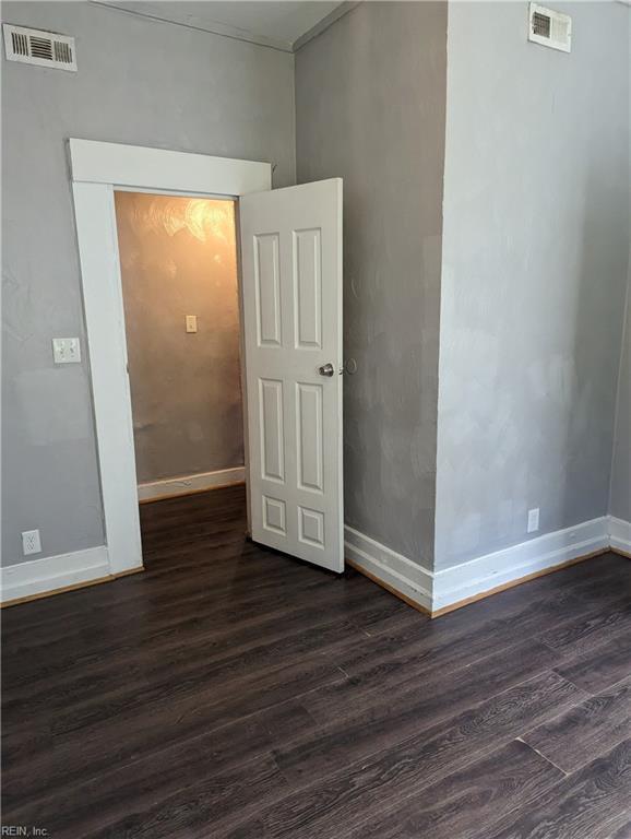 spare room featuring dark wood-style flooring, visible vents, and baseboards