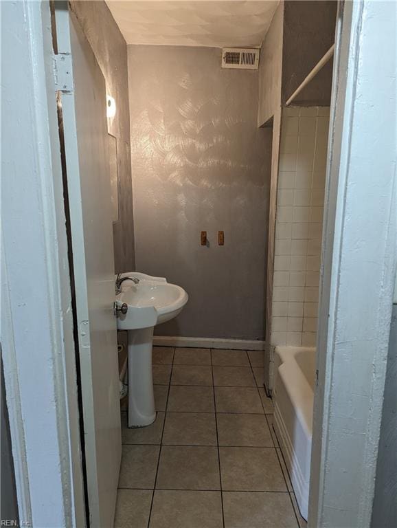 bathroom featuring baseboards, visible vents, tile patterned flooring, a washtub, and a sink