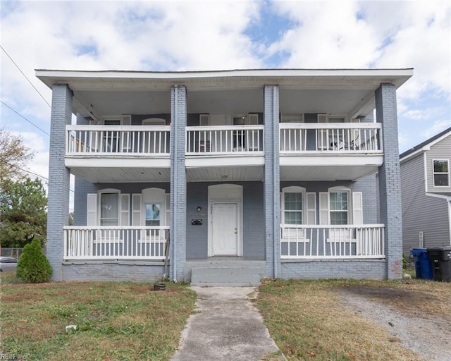 view of property with covered porch, brick siding, and a balcony