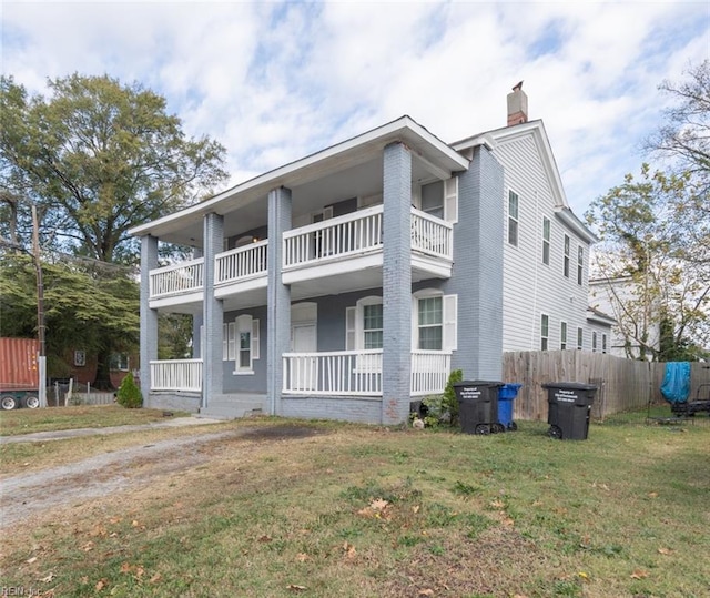 view of front of property with a chimney, a porch, fence, a balcony, and a front lawn