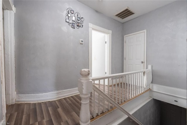 hall featuring visible vents, an upstairs landing, and wood finished floors