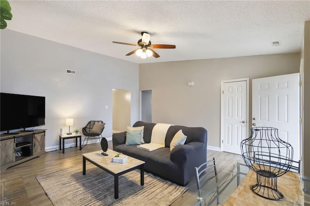 living area featuring visible vents, a ceiling fan, wood finished floors, vaulted ceiling, and a textured ceiling