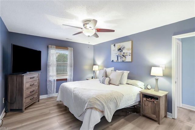 bedroom featuring a textured ceiling, light wood finished floors, a ceiling fan, and baseboards