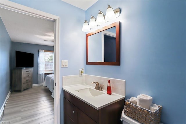 bathroom with baseboards, decorative backsplash, connected bathroom, wood finished floors, and vanity