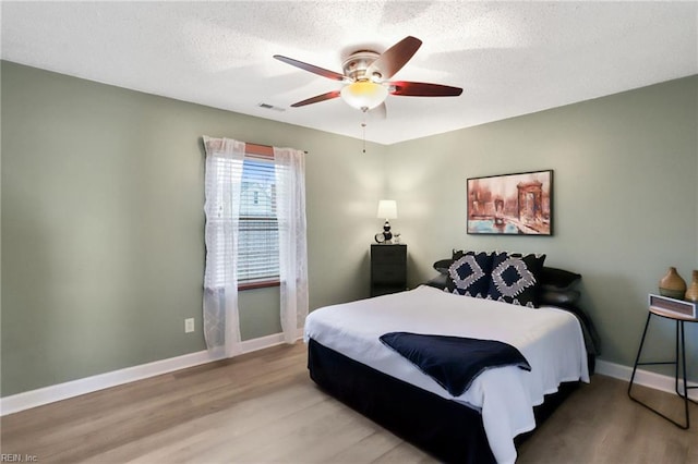 bedroom with a textured ceiling, wood finished floors, a ceiling fan, visible vents, and baseboards