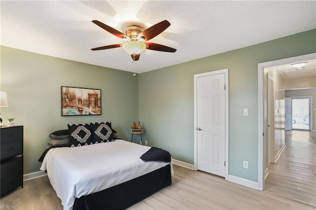 bedroom featuring a ceiling fan, light wood-type flooring, a textured ceiling, and baseboards