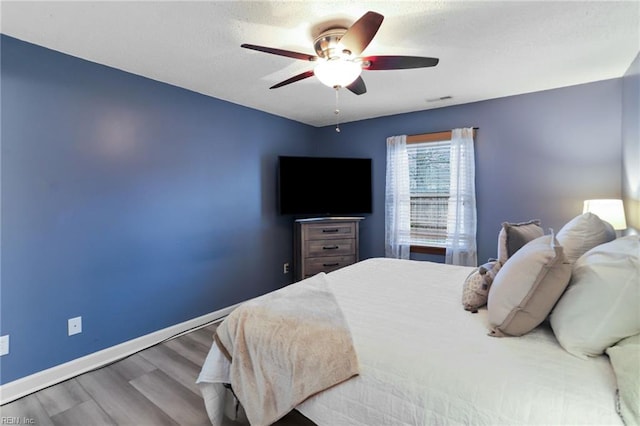 bedroom with a ceiling fan, a textured ceiling, baseboards, and wood finished floors