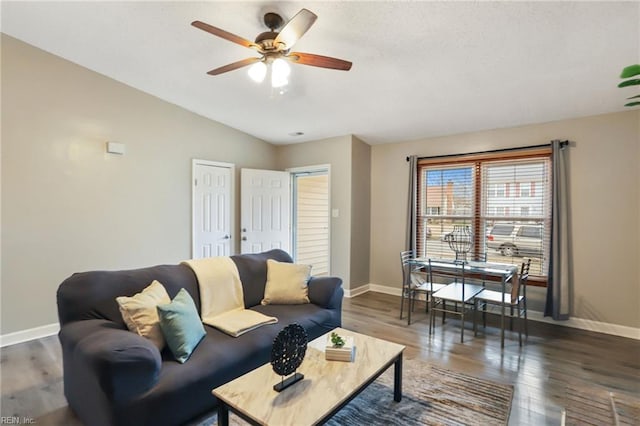 living room featuring lofted ceiling, dark wood-style floors, baseboards, and a ceiling fan