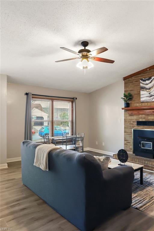 living room with a textured ceiling, ceiling fan, wood finished floors, baseboards, and a brick fireplace