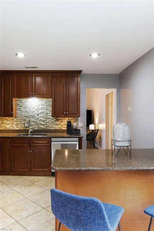 kitchen with dark stone countertops, backsplash, a sink, and light tile patterned flooring