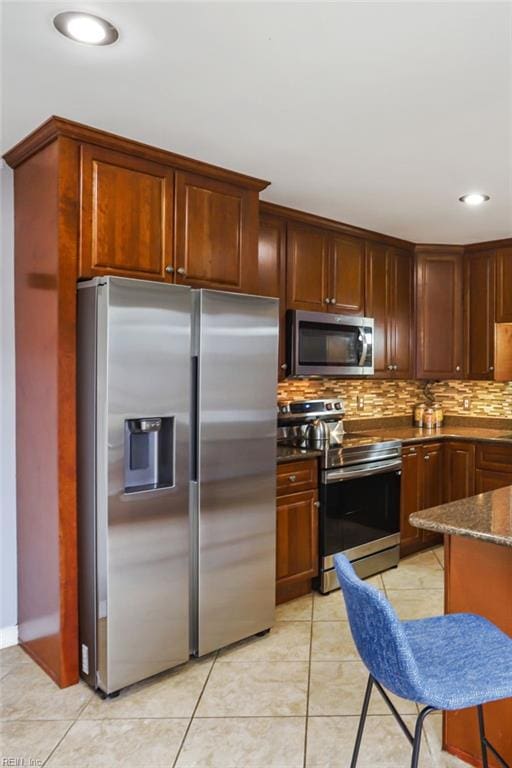 kitchen featuring stainless steel appliances, light tile patterned floors, dark stone countertops, and tasteful backsplash