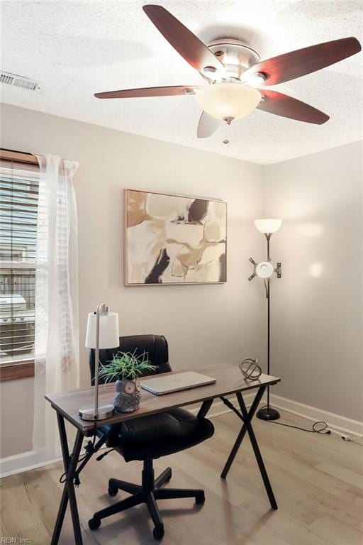 office with light wood-style floors, baseboards, visible vents, and a textured ceiling