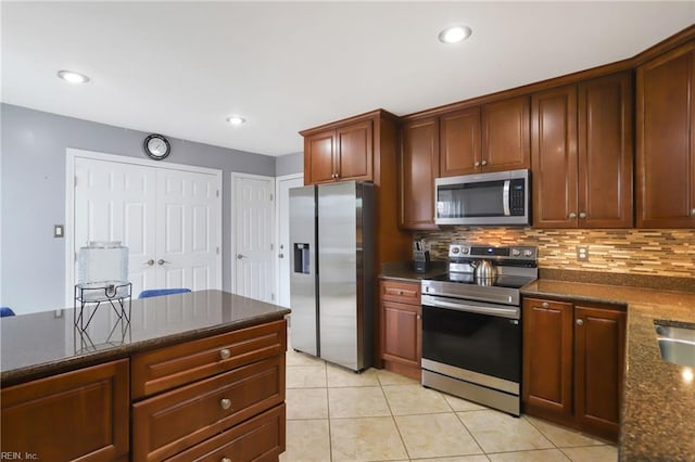 kitchen with light tile patterned floors, appliances with stainless steel finishes, decorative backsplash, and dark stone countertops