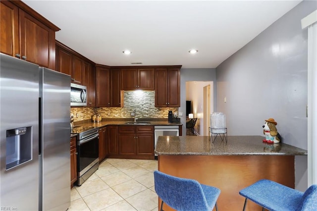 kitchen with light tile patterned floors, stainless steel appliances, backsplash, a sink, and a peninsula