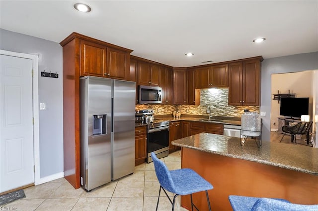 kitchen with a breakfast bar, decorative backsplash, appliances with stainless steel finishes, light tile patterned flooring, and a sink