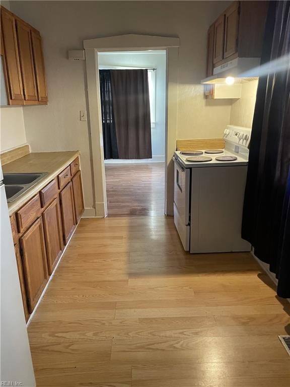 kitchen with light wood-style flooring, a sink, under cabinet range hood, white electric range, and brown cabinets