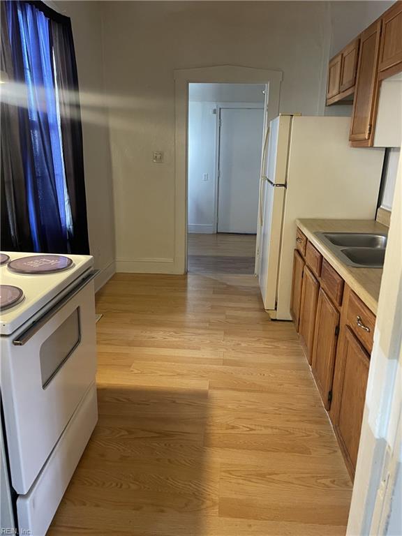 kitchen with white electric range oven, brown cabinetry, a sink, light countertops, and light wood-type flooring