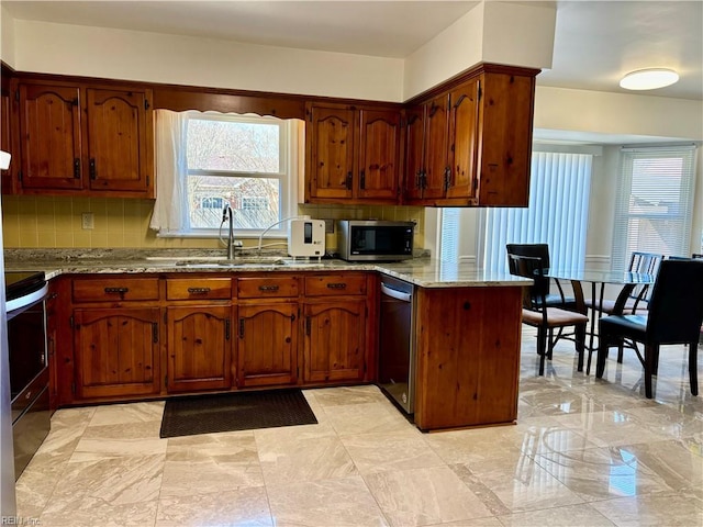 kitchen featuring a peninsula, a sink, appliances with stainless steel finishes, light stone countertops, and tasteful backsplash