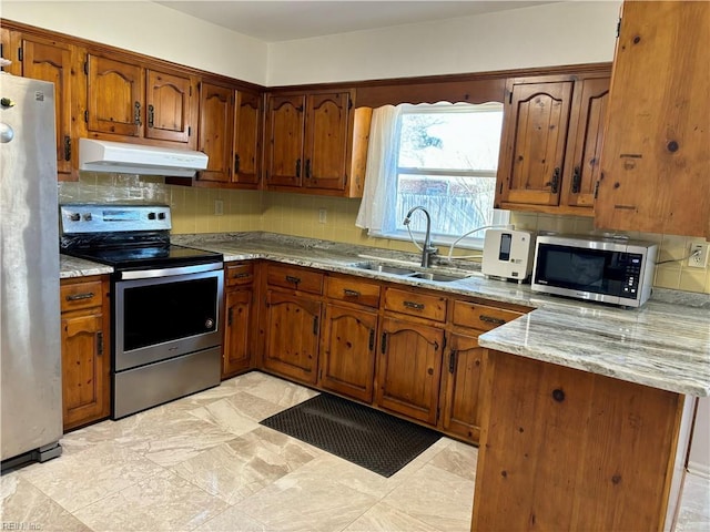 kitchen featuring brown cabinetry, a peninsula, stainless steel appliances, under cabinet range hood, and a sink