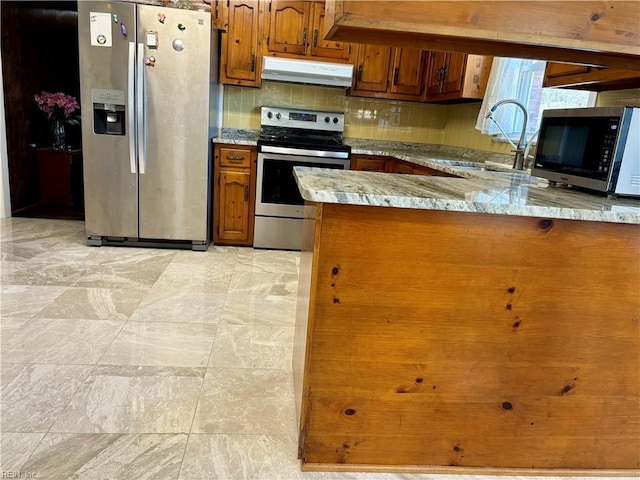 kitchen with under cabinet range hood, stainless steel appliances, a sink, backsplash, and brown cabinetry