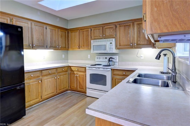 kitchen with light wood-style flooring, white appliances, a skylight, a sink, and light countertops