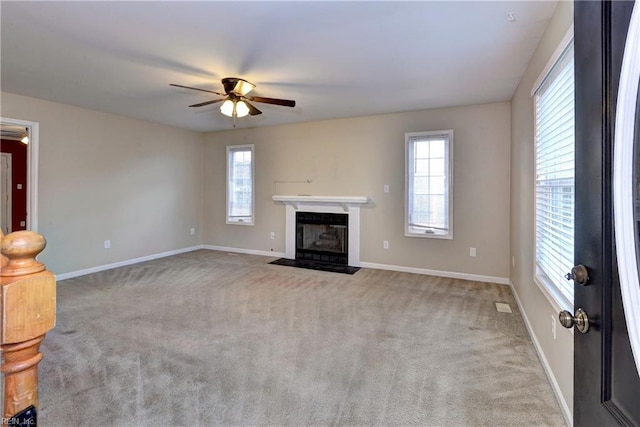 unfurnished living room featuring a wealth of natural light, carpet, a fireplace with flush hearth, and a ceiling fan