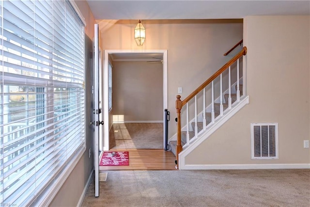 carpeted foyer featuring stairway, visible vents, and baseboards