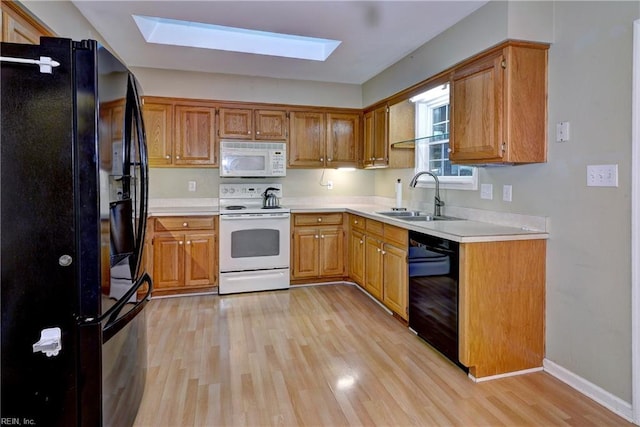 kitchen with a skylight, light countertops, light wood-style flooring, a sink, and black appliances